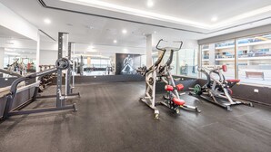 A gym with various exercise equipment, large windows, and a mirrored wall. - Free Housekeeping Visits During Your Stay - Stayshort - Cozy Studio in Sposrt City That Sleeps 3 (Dubai)
