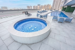 Tagpool med jacuzzi, liggestole og udsigt over bybilledet.