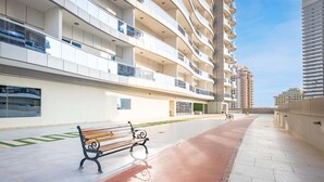 A multi-story residential building with balconies, a paved walkway, and a bench. - Free Housekeeping Visits During Your Stay - Stayshort - Cozy Studio in Sposrt City That Sleeps 3 (Dubai)