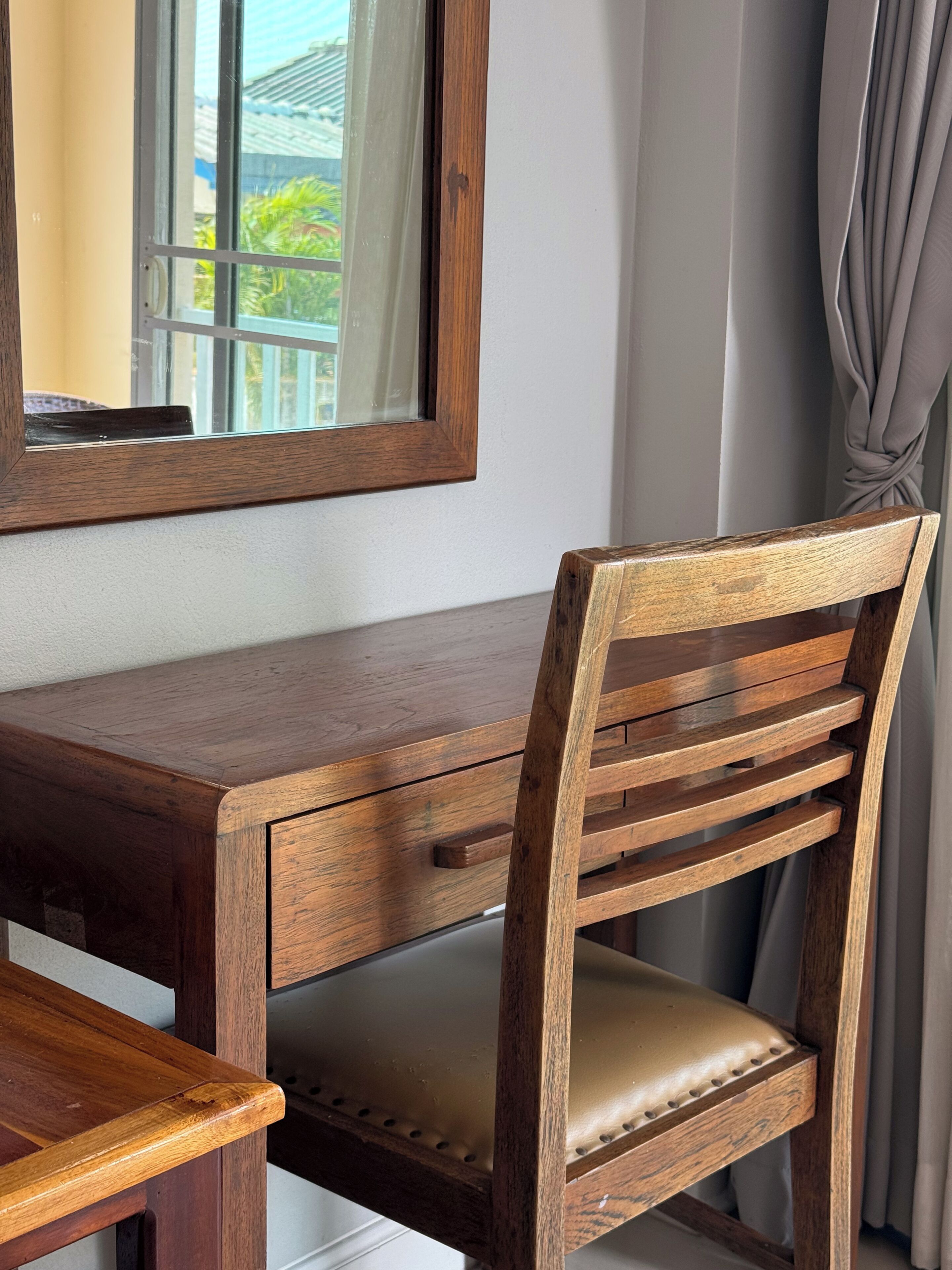 A wooden desk with a chair, a mirror, and a window with curtains.
