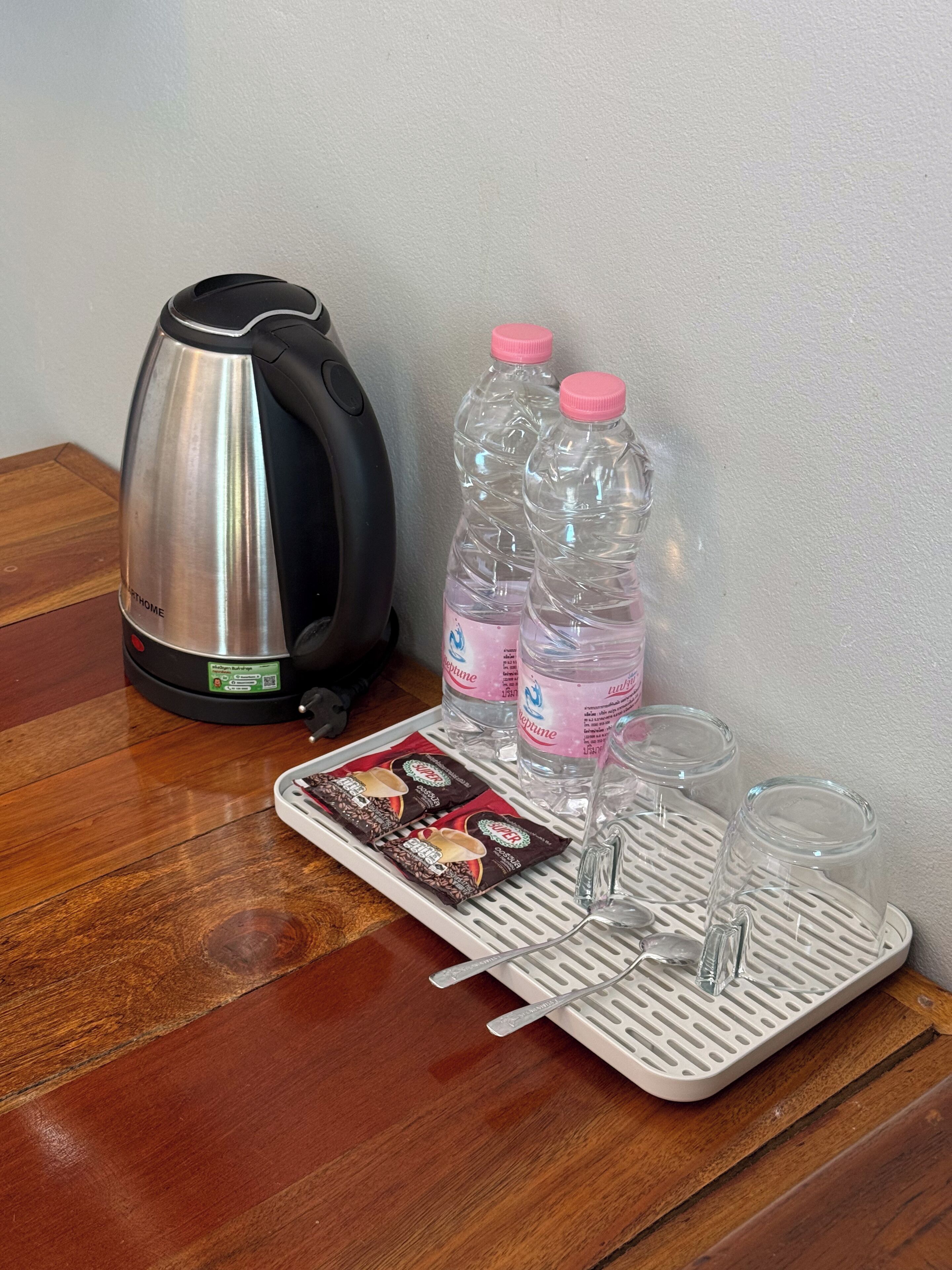 A coffee maker, two water bottles, a tray with coffee pods, and two glasses on a wooden table.