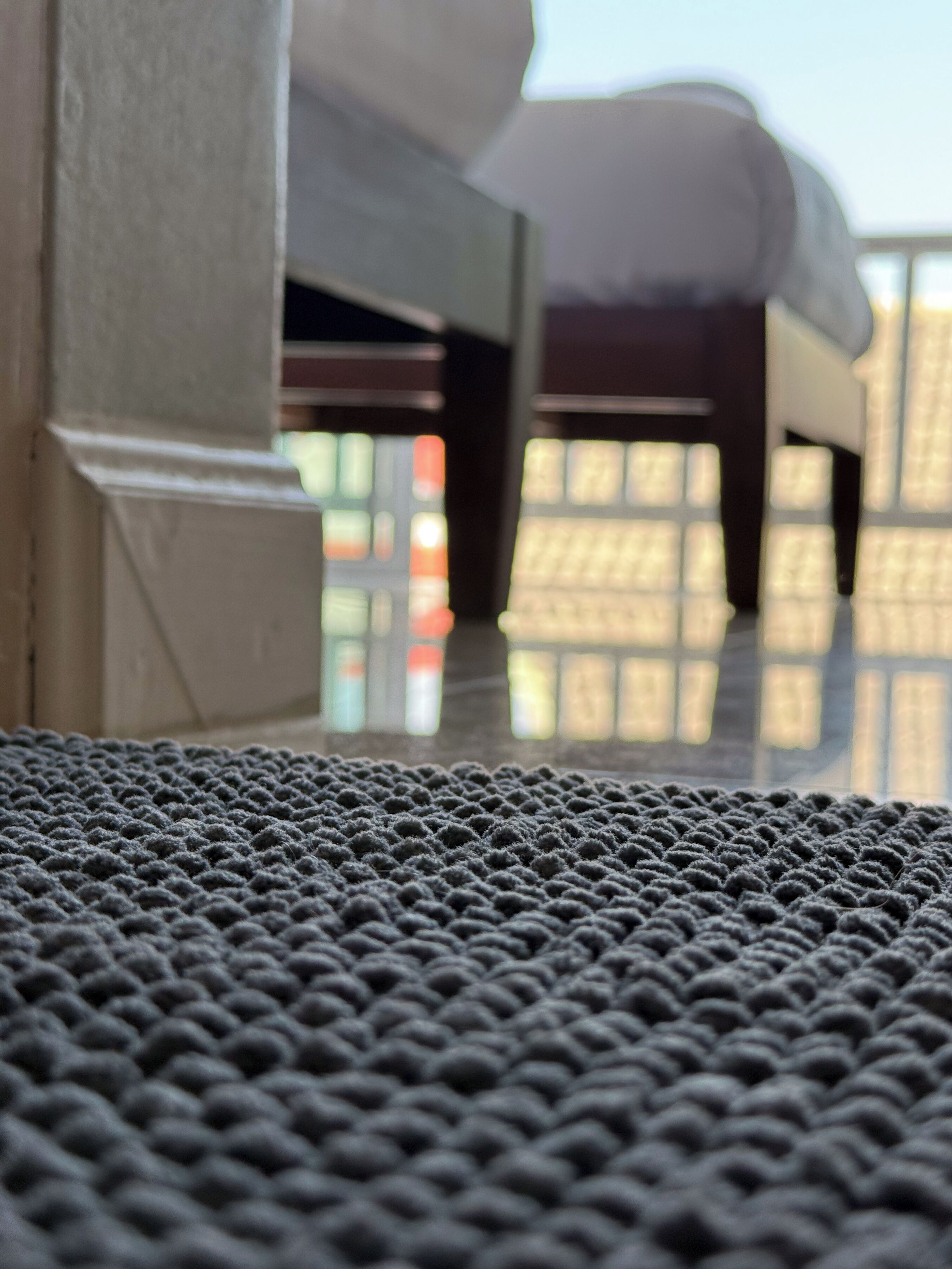 Une moquette à motifs géométriques et à texture prononcée, une colonne blanche et un arrière-plan flou avec une fenêtre.