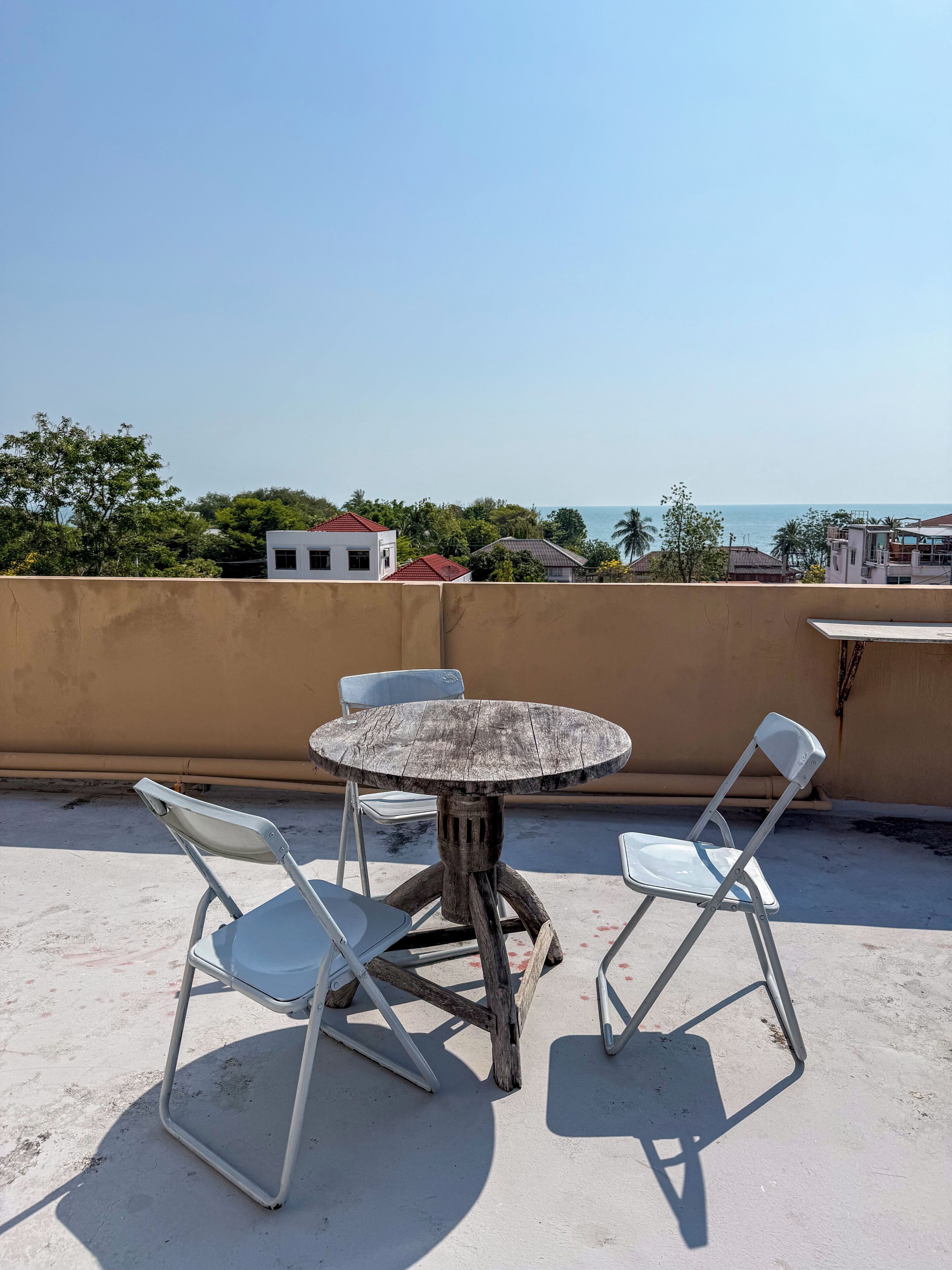 Eine Dachterrasse mit rundem Tisch und vier Stühlen, mit Blick auf eine Küstenlandschaft mit Gebäuden und Bäumen.