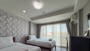 Une chambre d’hôtel avec deux lits, une grande fenêtre avec des rideaux, un luminaire au plafond et un climatiseur fixé au mur.