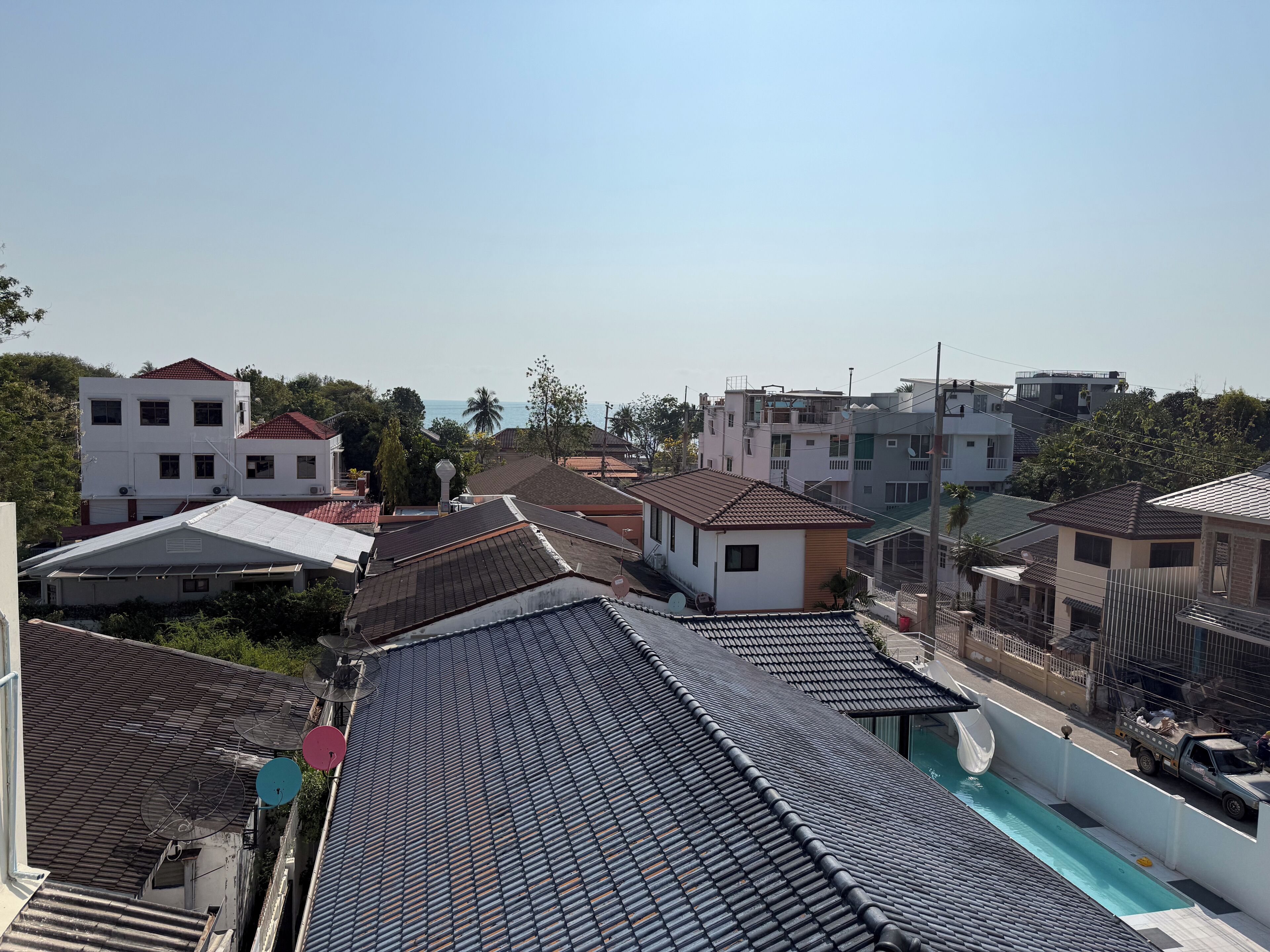 Zona residencial con varias casas, una piscina y vistas despejadas al mar.
