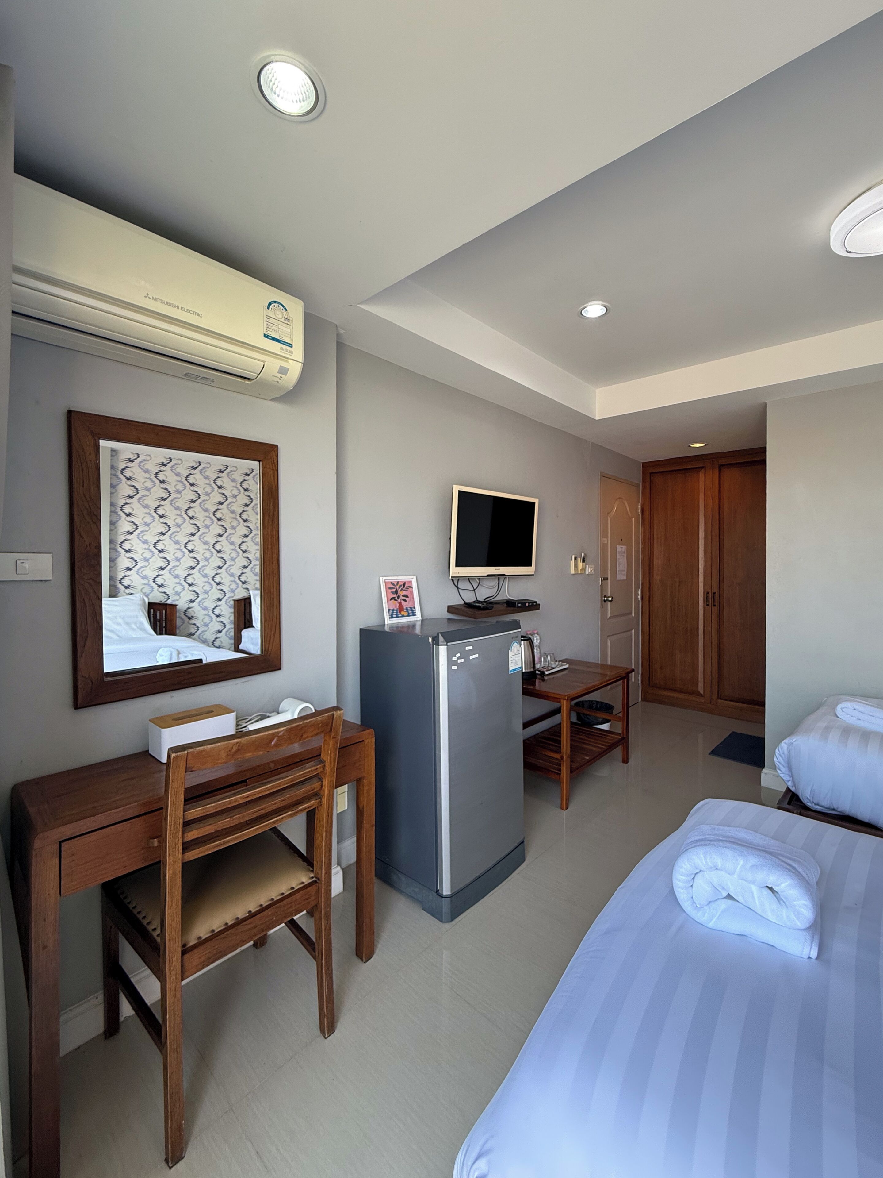 A hotel room with a bed, a desk with a chair, a television, a refrigerator, and a wardrobe.