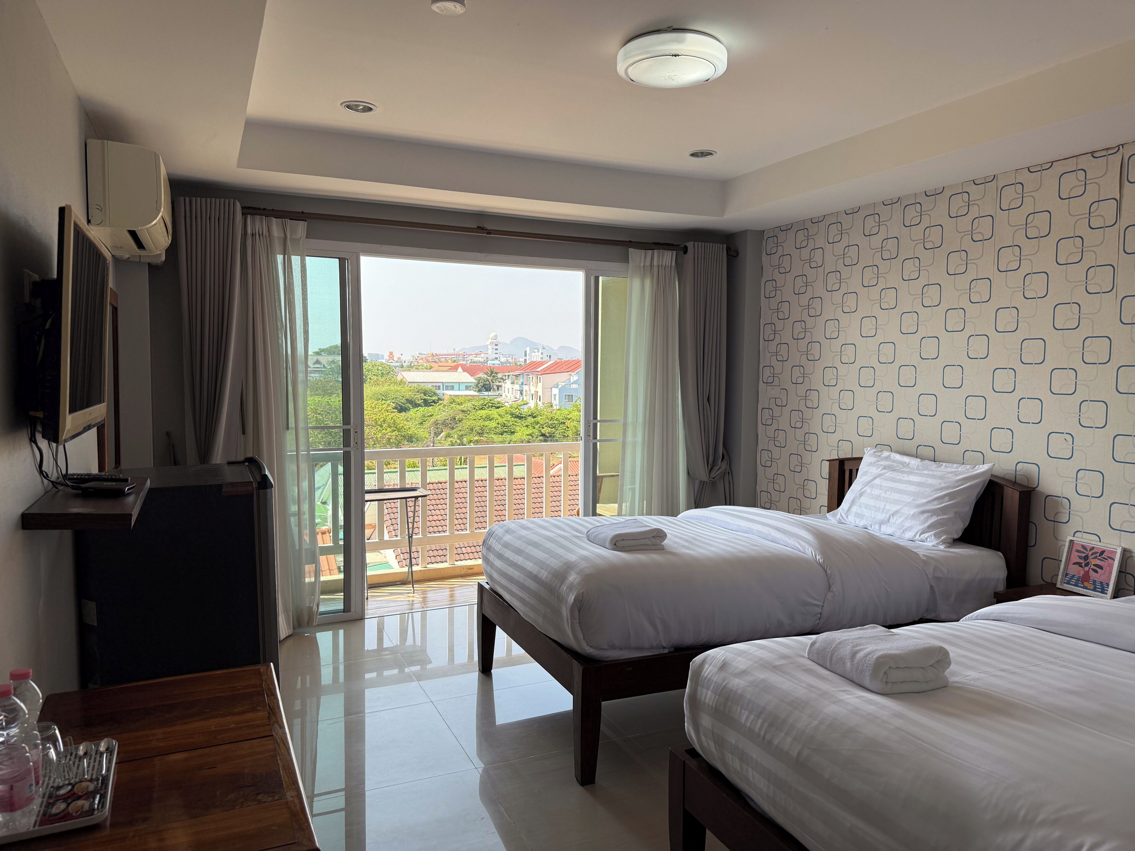 A hotel room with two beds, a TV, a desk, and a balcony with a view.
