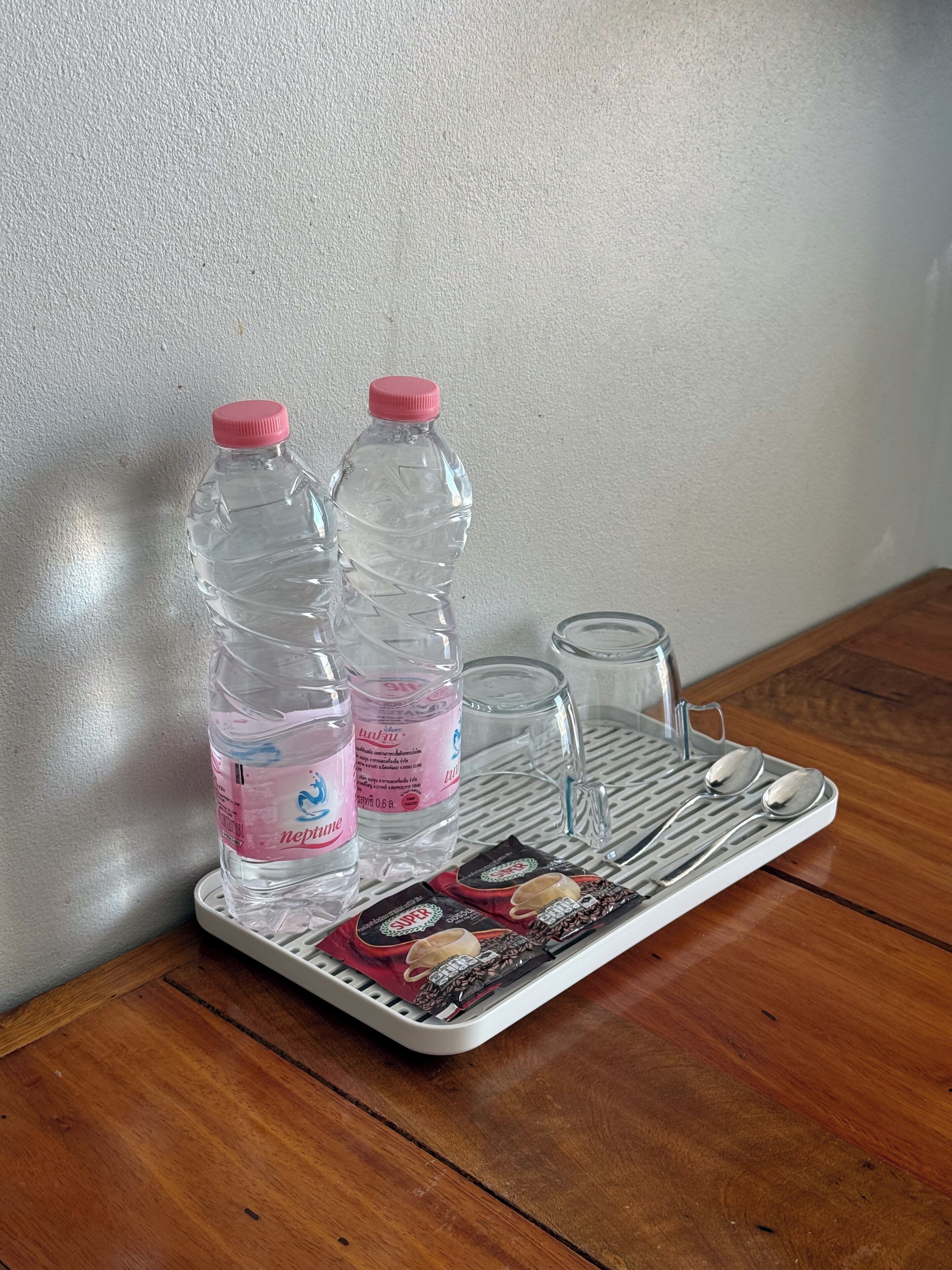 Una bandeja con dos botellas de agua y un vaso sobre una mesa de madera frente a una pared con textura.
