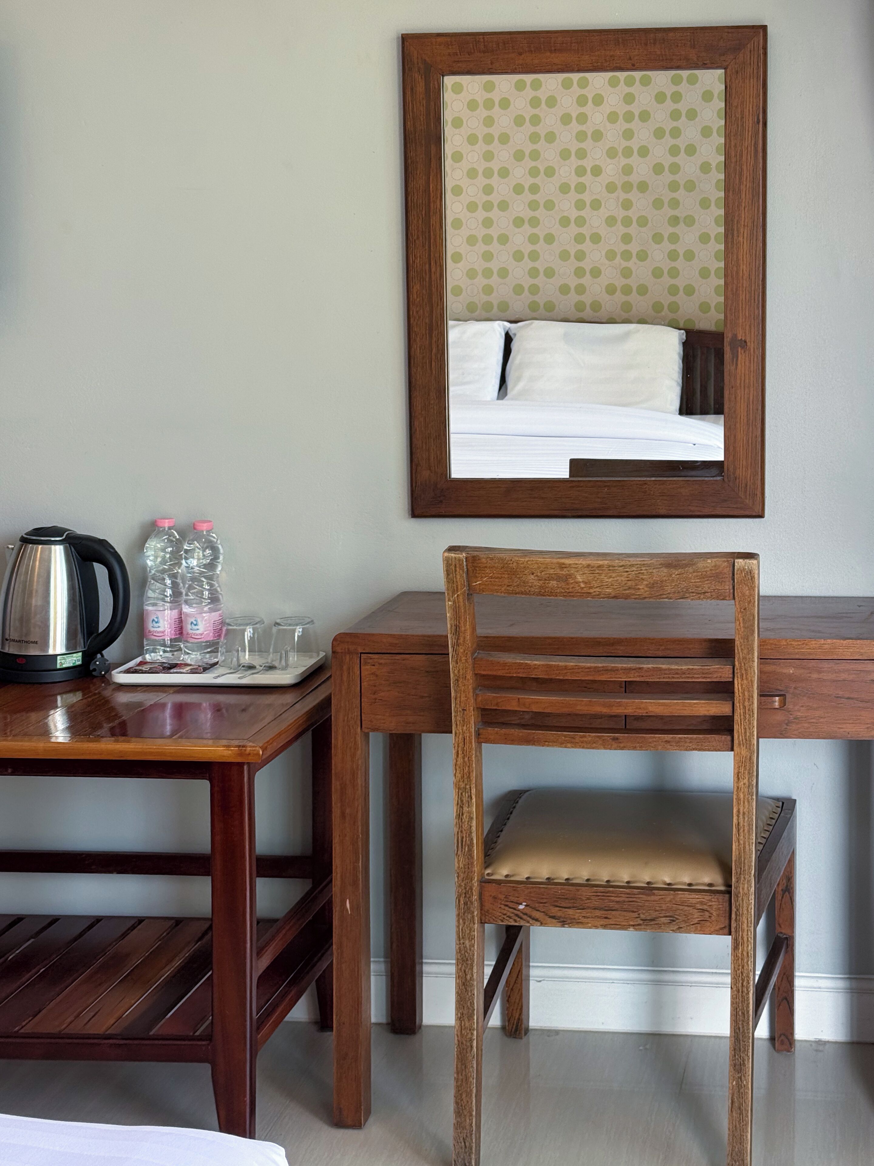 A wooden desk with a chair, a mirror, a kettle, and water bottles.