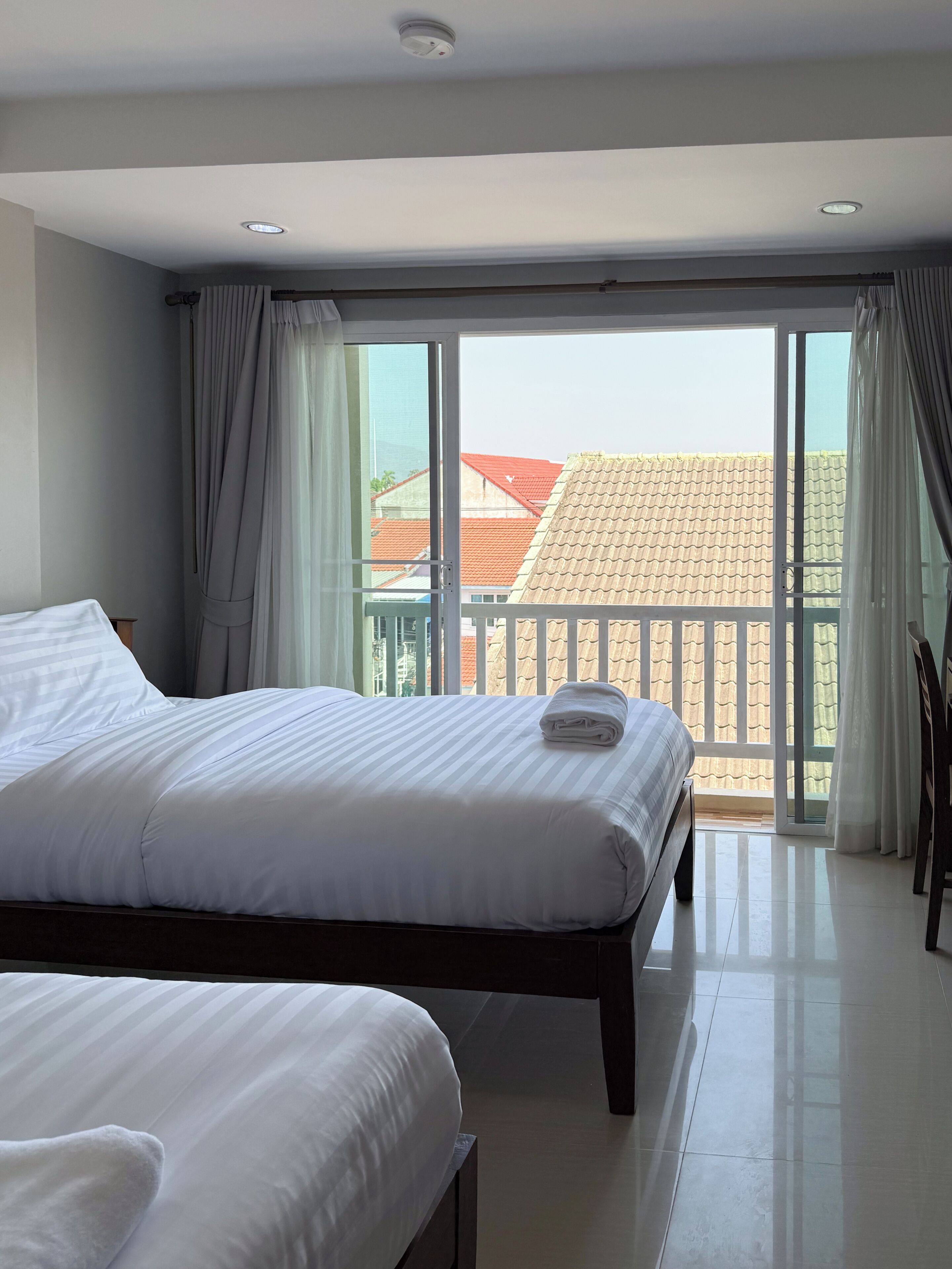 Een hotelkamer met een groot bed, een kleiner bed en een balkon met uitzicht op gebouwen.