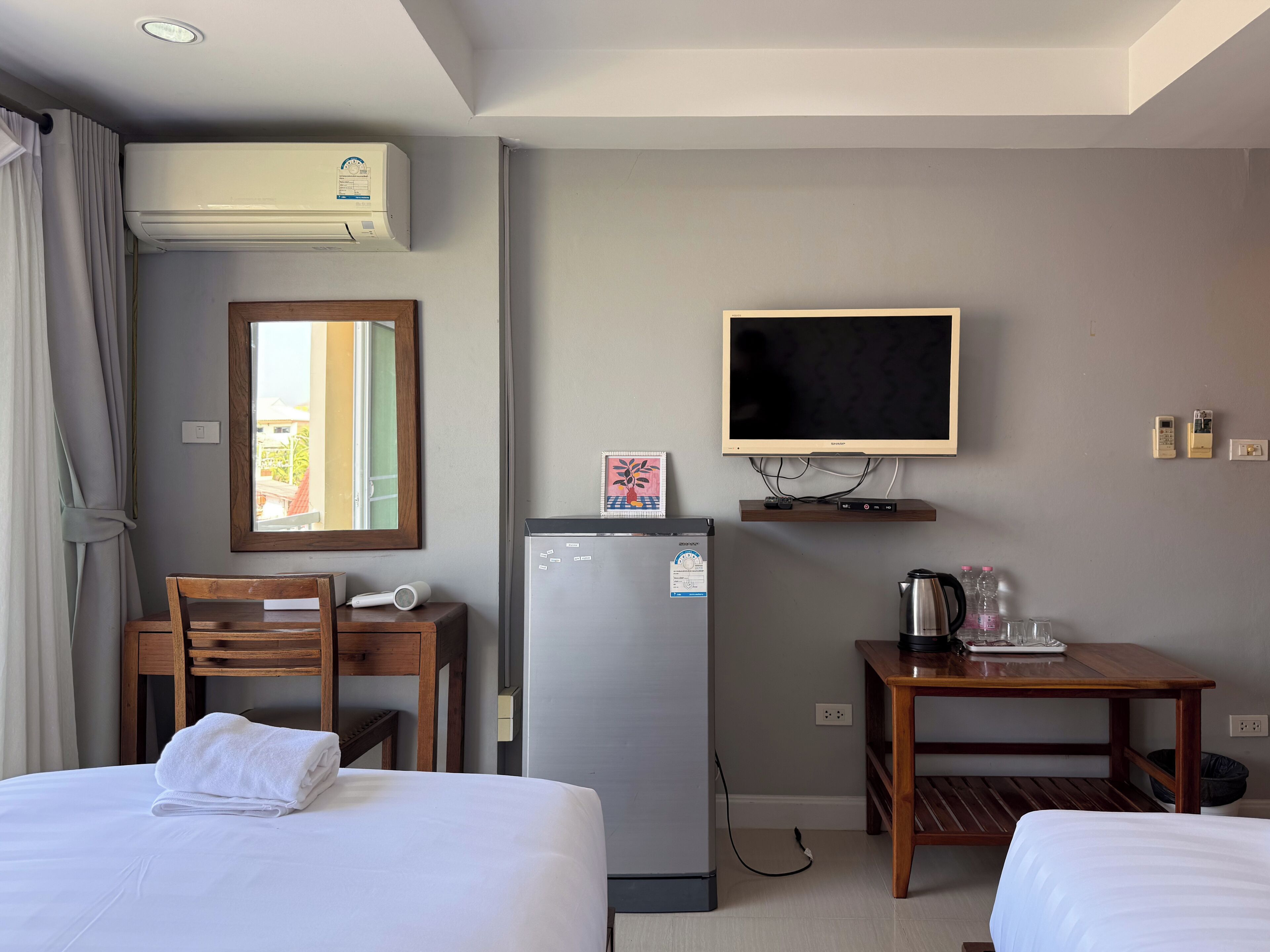 A hotel room with a bed, a desk with a chair, a refrigerator, a television, and an air conditioning unit.