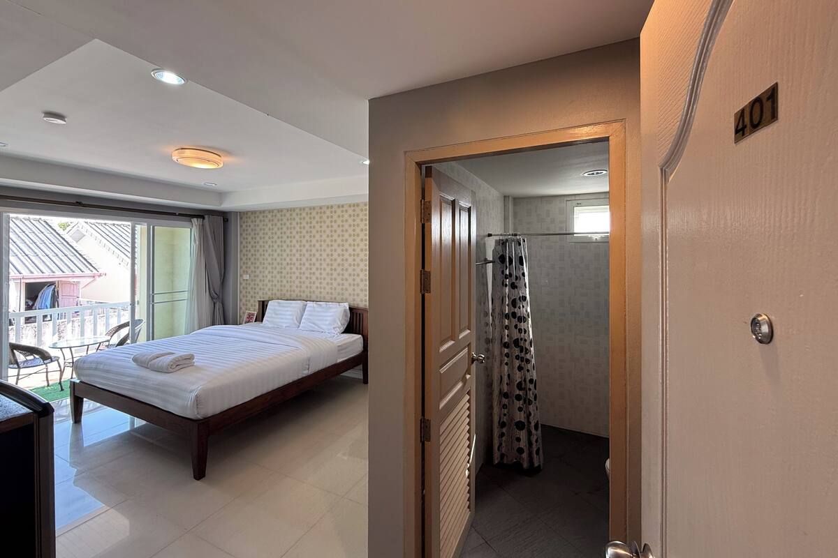 Une chambre d’hôtel avec un lit, une salle de bain avec un rideau de douche et un balcon avec une chaise.