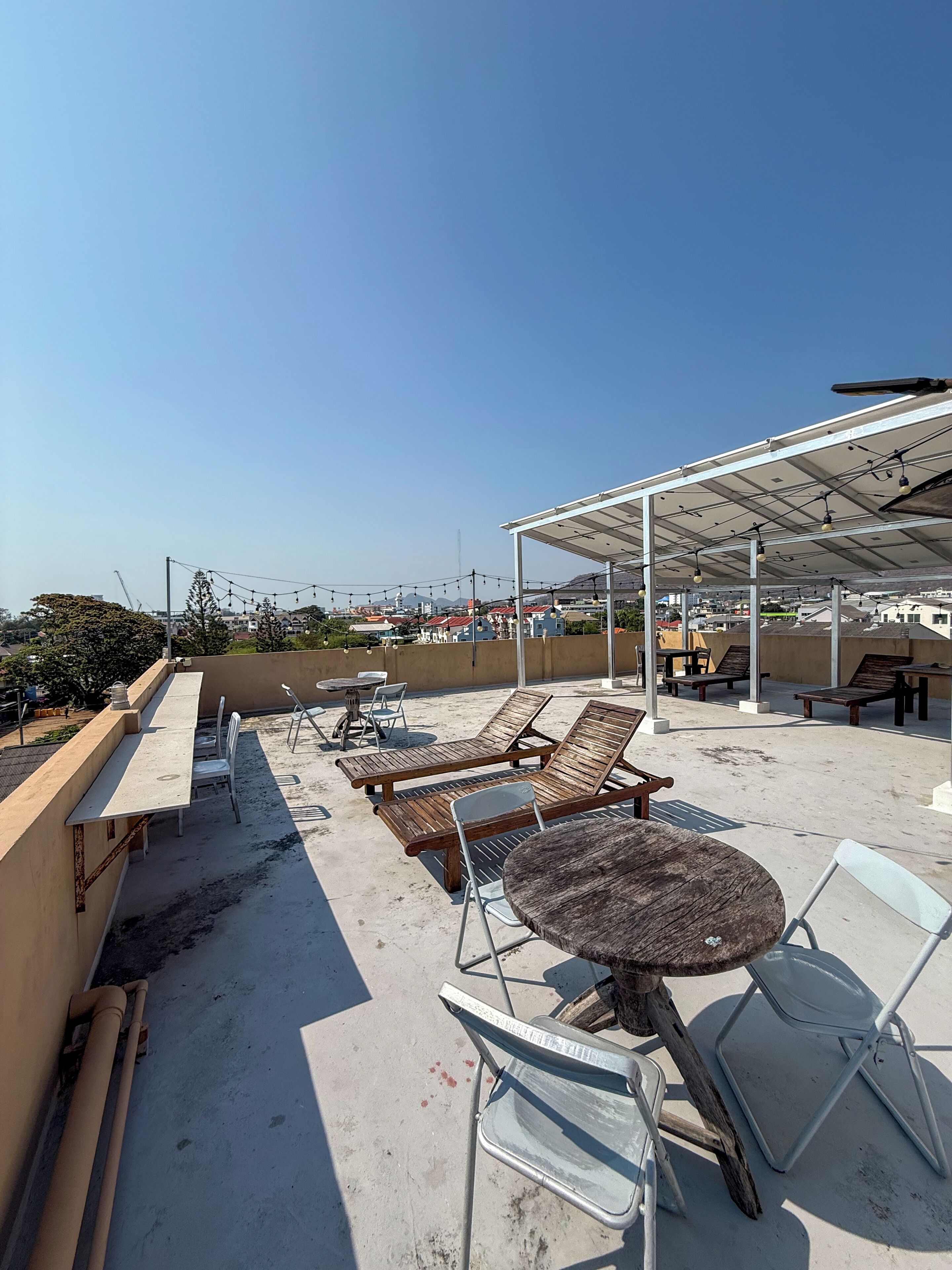 A rooftop terrace with lounge chairs, a table, and a covered area with string lights.