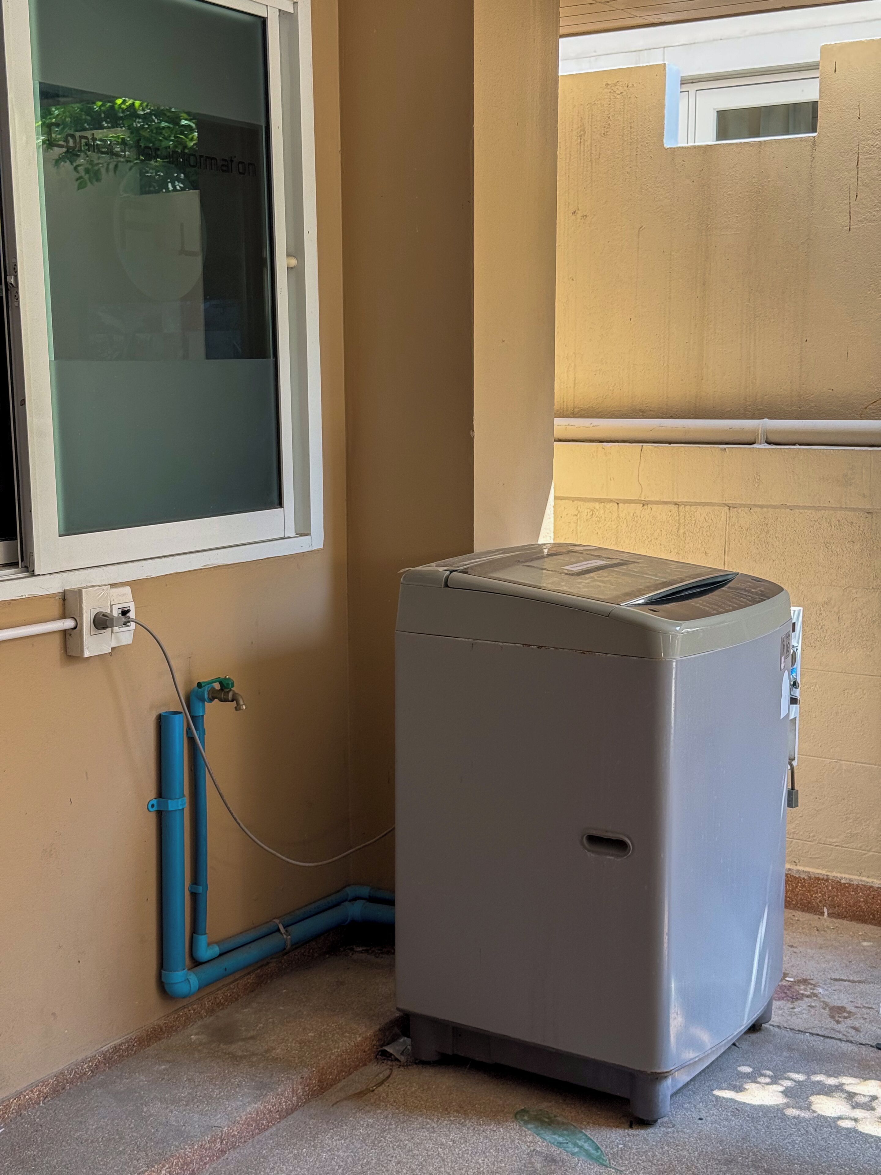 Eine kompakte, graue tragbare Klimaanlage, an einer beigen Wand montiert, verbunden mit einem blauen PVC-Rohr und einer Steckdose.