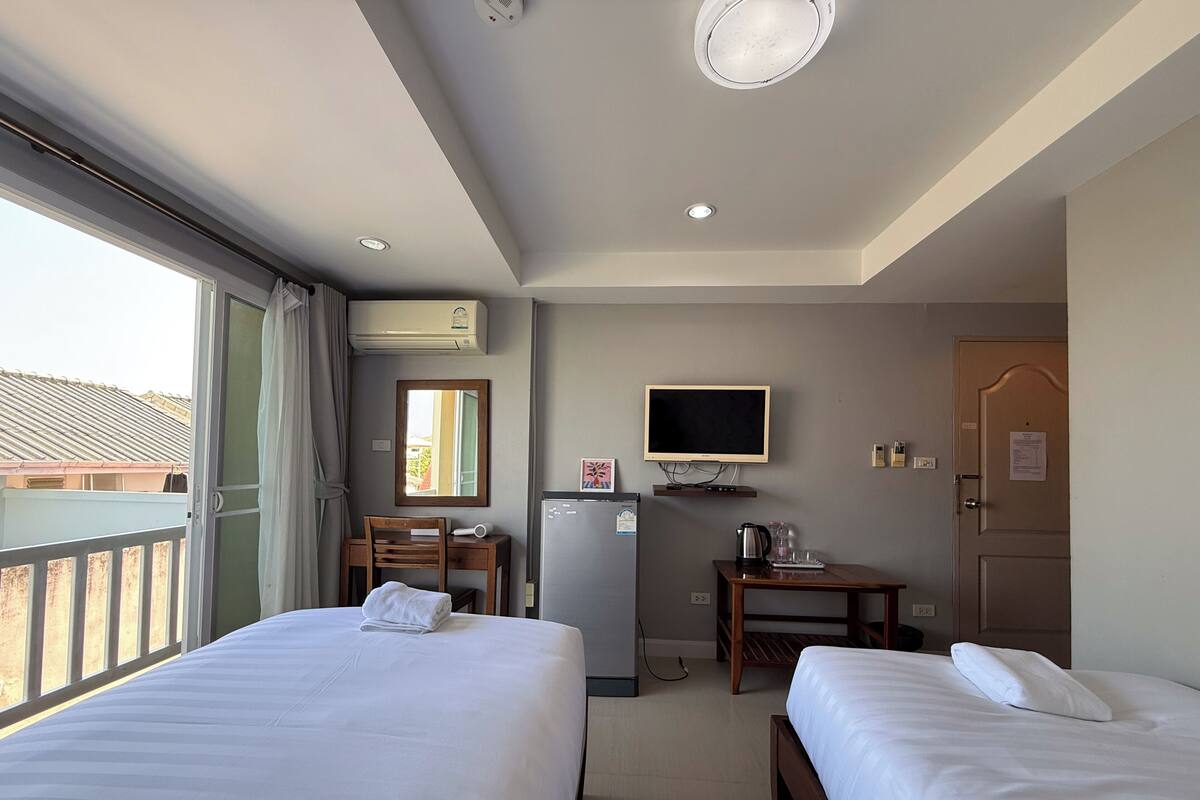 Une chambre d’hôtel avec deux lits, un bureau avec un ordinateur, une télévision et un appareil de climatisation.