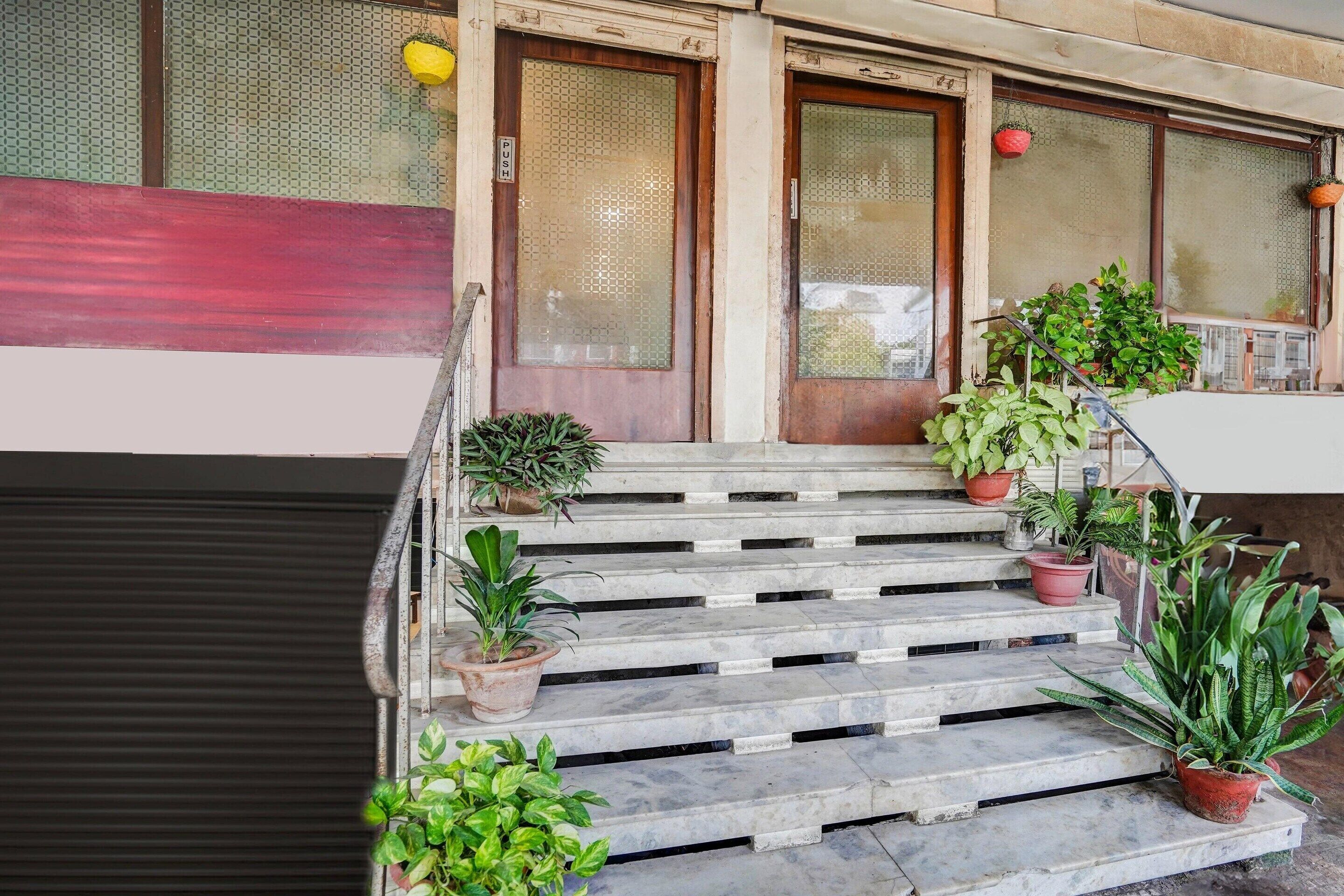 A set of marble steps leading to a door with a red panel, flanked by two windows with frosted glass and hanging plants.