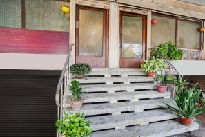 Un conjunto de escalones de mármol que conducen a una puerta con panel rojo, flanqueada por dos ventanas con vidrio esmerilado y plantas colgantes.