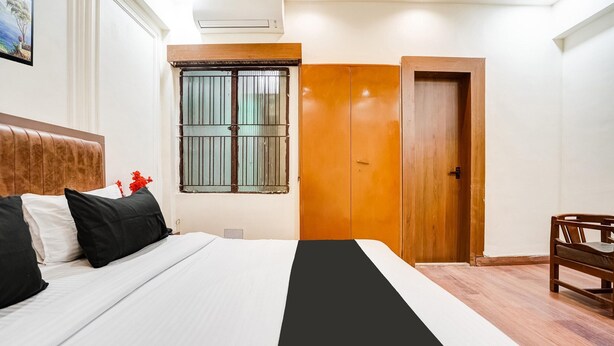 Un dormitorio con cama, un armario de madera, una ventana con rejas y una puerta.
