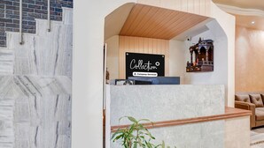 Un área de recepción con piso de mármol, mostrador de recepción, techo de madera, espejo montado en la pared y un sofá de cuero marrón.