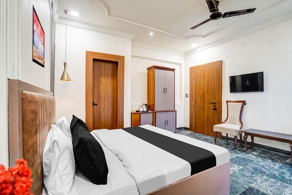 Una habitación de hotel con cama, armario de madera, televisor, banco y ventilador de techo.