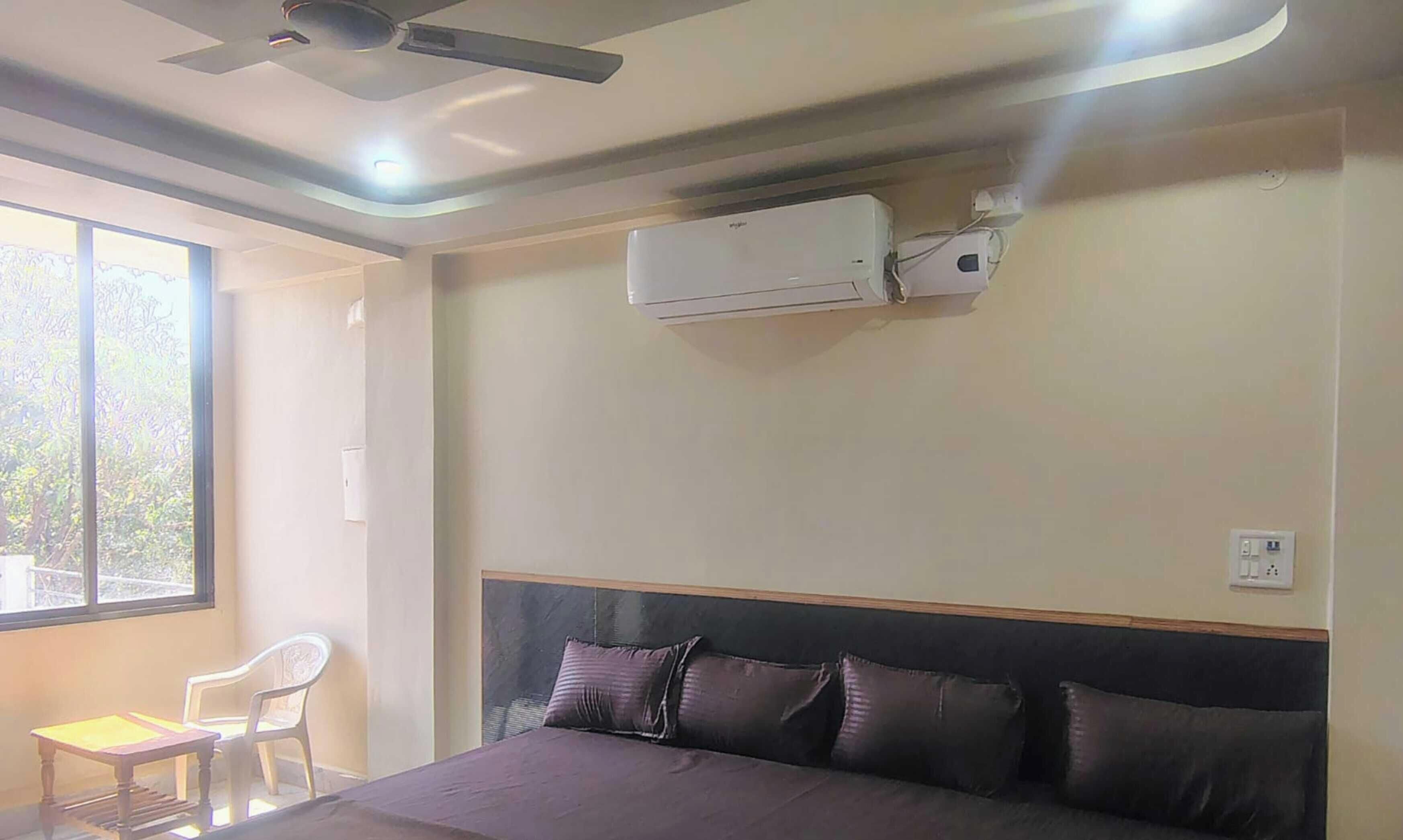 A room with a bed, a ceiling fan, an air conditioner, a window with a view, and a chair.