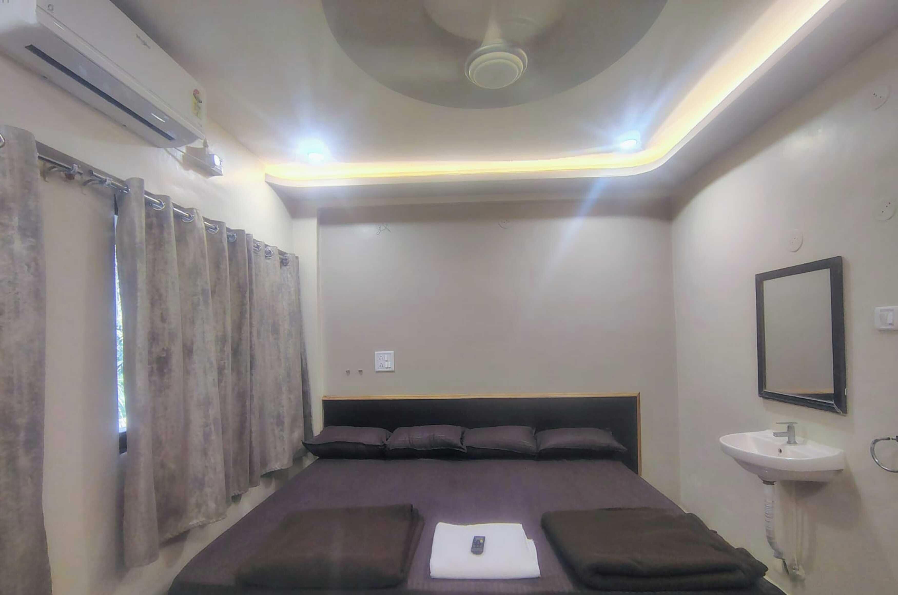 A hotel room with a bed, a bedside table, a wall-mounted sink, and a ceiling fan.