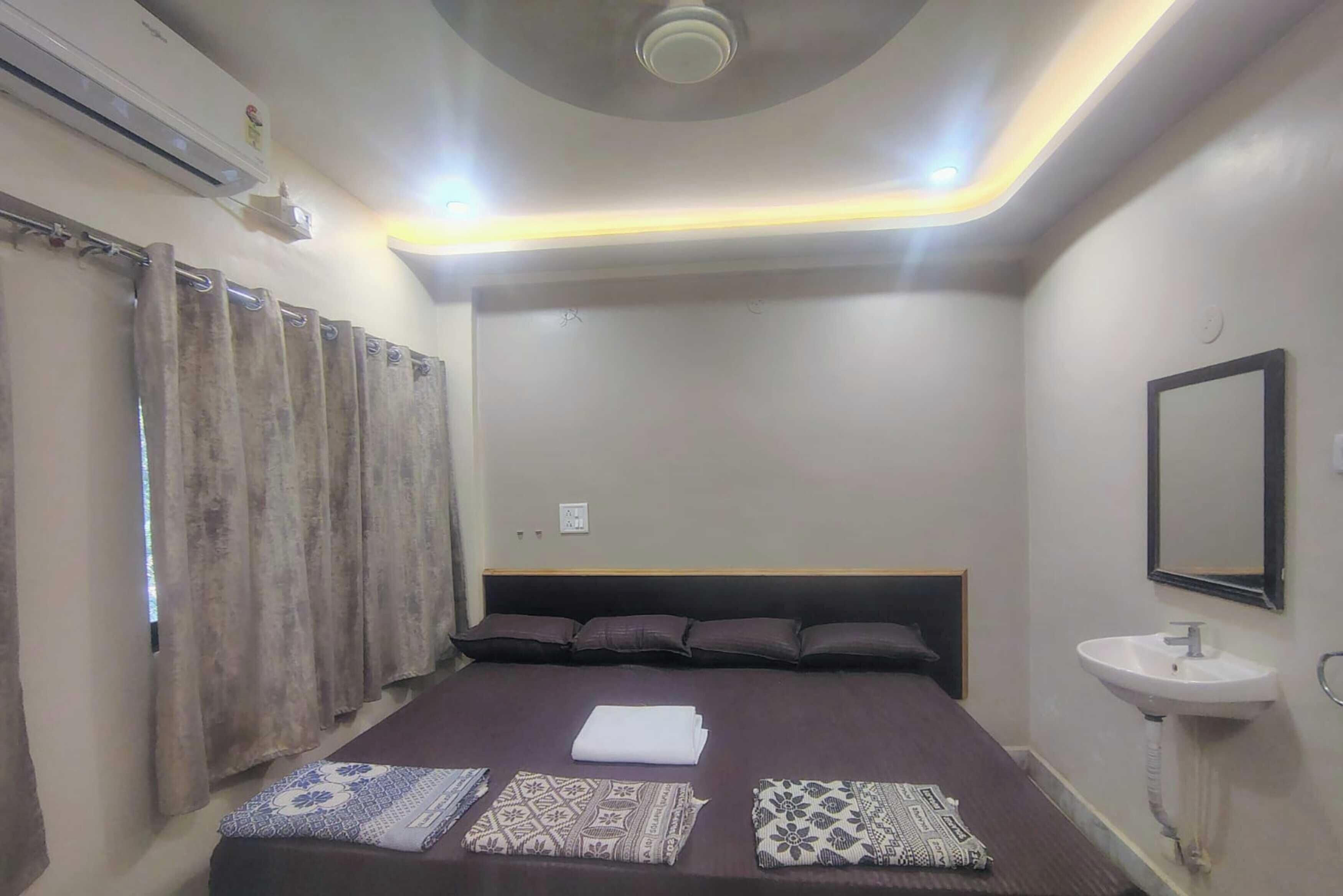 Quarto com cama, cortinas, mesa de cabeceira, espelho fixado na parede e luminária de teto.