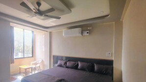 A hotel room with a bed, a ceiling fan, an air conditioning unit, a small table, and a chair.