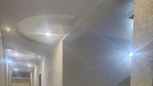 A hallway with a staircase, a ceiling with recessed lighting, and a door leading to another room.