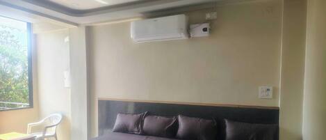 Ein Schlafzimmer mit einem Bett, einem Fenster, einem Sessel und einer Klimaanlage.