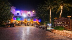 A hotel entrance with a sign reading 'SHIVSAGAR HOME STAY' and a paved driveway leading to the building.