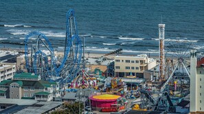 Un parque de atracciones costero con montañas rusas, una noria y una playa al fondo.