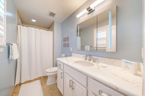 Une salle de bain avec un rideau de douche, des toilettes, un meuble-lavabo avec un évier et un grand miroir.