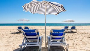 Ein Strand mit zwei Reihen aus blauen und weißen Liegestühlen und gestreiften Sonnenschirmen.