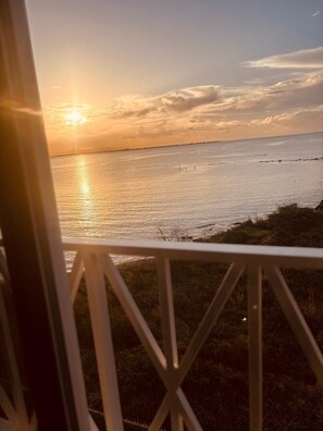 Vista di un tramonto sul mare calmo da un balcone con ringhiera.