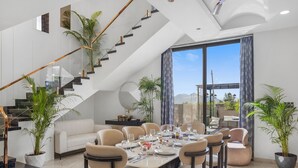 A modern dining area with a high ceiling, a staircase, and large windows. - ELIVAAS Shreya Blossom 4 BHK With Pool (Udaipur)