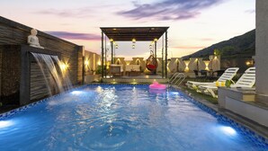 A swimming pool with a waterfall feature, lounge chairs, and a Buddha statue. - ELIVAAS Shreya Blossom 4 BHK With Pool (Udaipur)