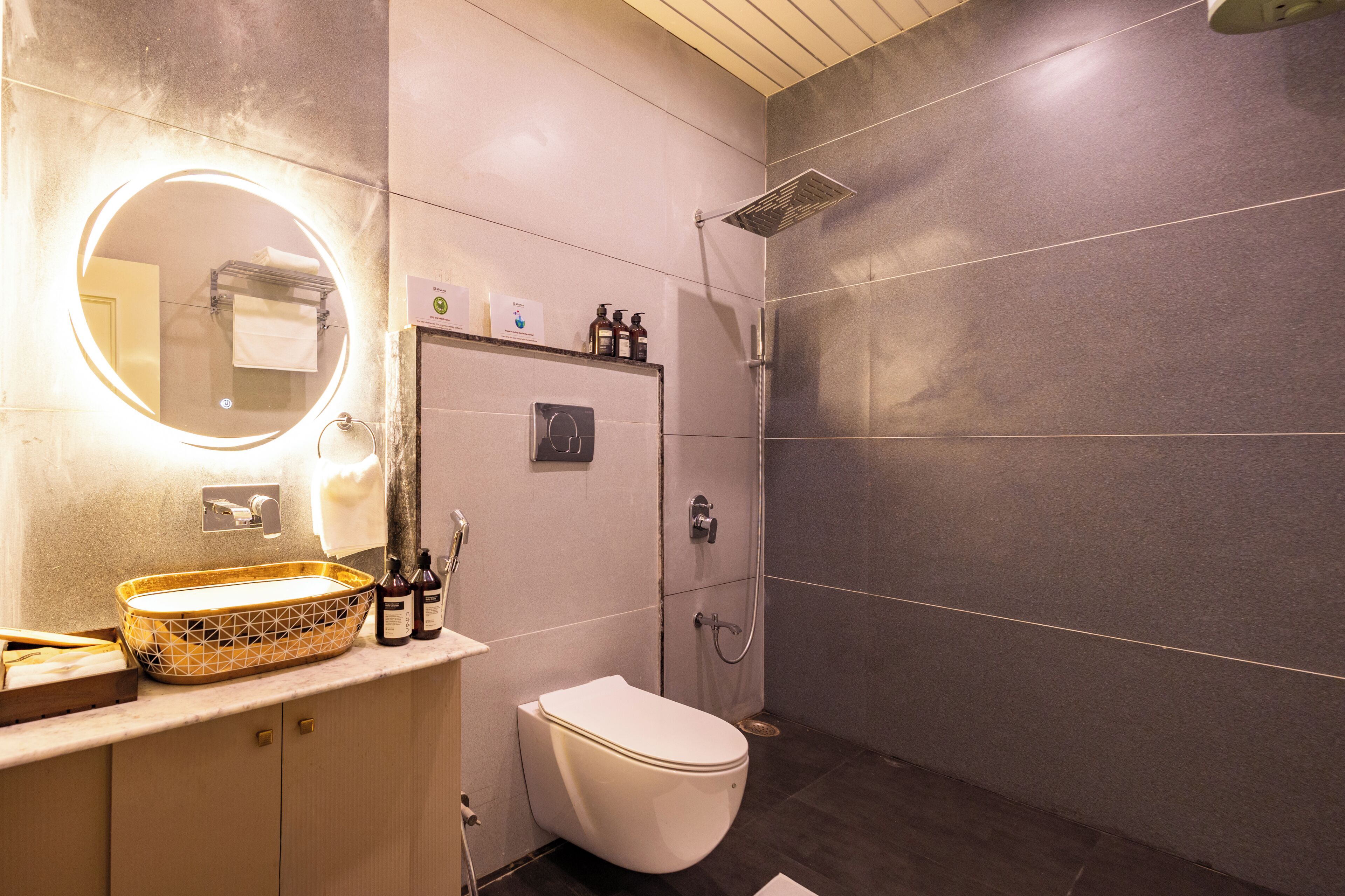 Un baño con un espejo redondo, un inodoro, una ducha y un lavabo con botellas.