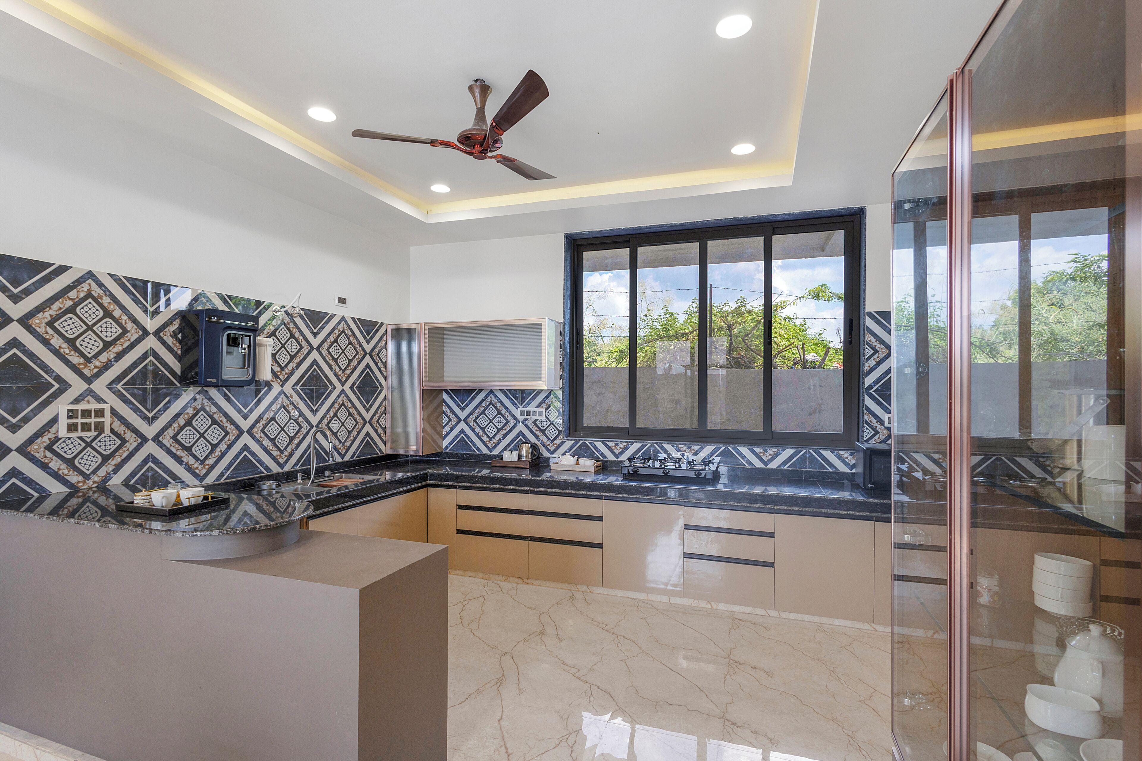 A modern kitchen with a built-in water dispenser, a ceiling fan, and a large window with a view of greenery.