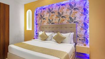 A bedroom with a bed, a headboard with floral wallpaper, and a bedside table with a lamp.