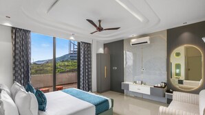 A bedroom with a bed, a vanity, a mirror, and a balcony with a view. - ELIVAAS Shreya Blossom 4 BHK With Pool (Udaipur)