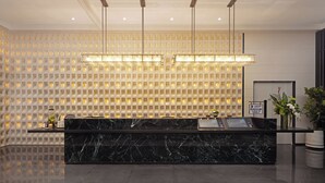 Zona de recepción con mostrador de mármol, iluminación colgante, mostrador de recepción y un panel decorativo con luces.