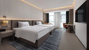 Una habitación de hotel moderna con dos camas, un escritorio, una silla y un ventanal amplio.