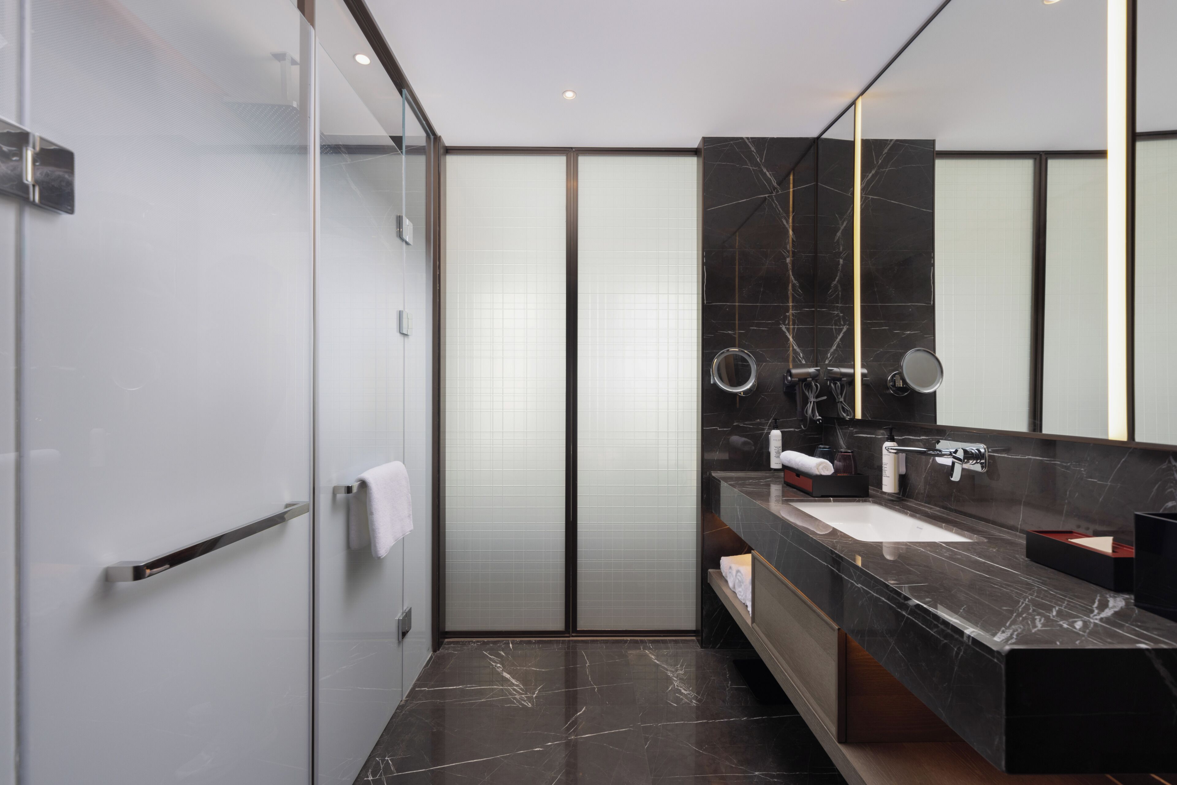 Een moderne badkamer met een douchecabine van glas, een wastafel met marmeren blad en een grote spiegel.