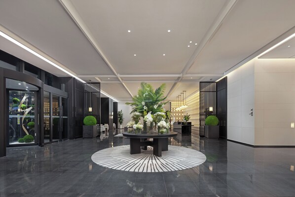 A modern lobby with a central round table, glass doors, and a reception desk.