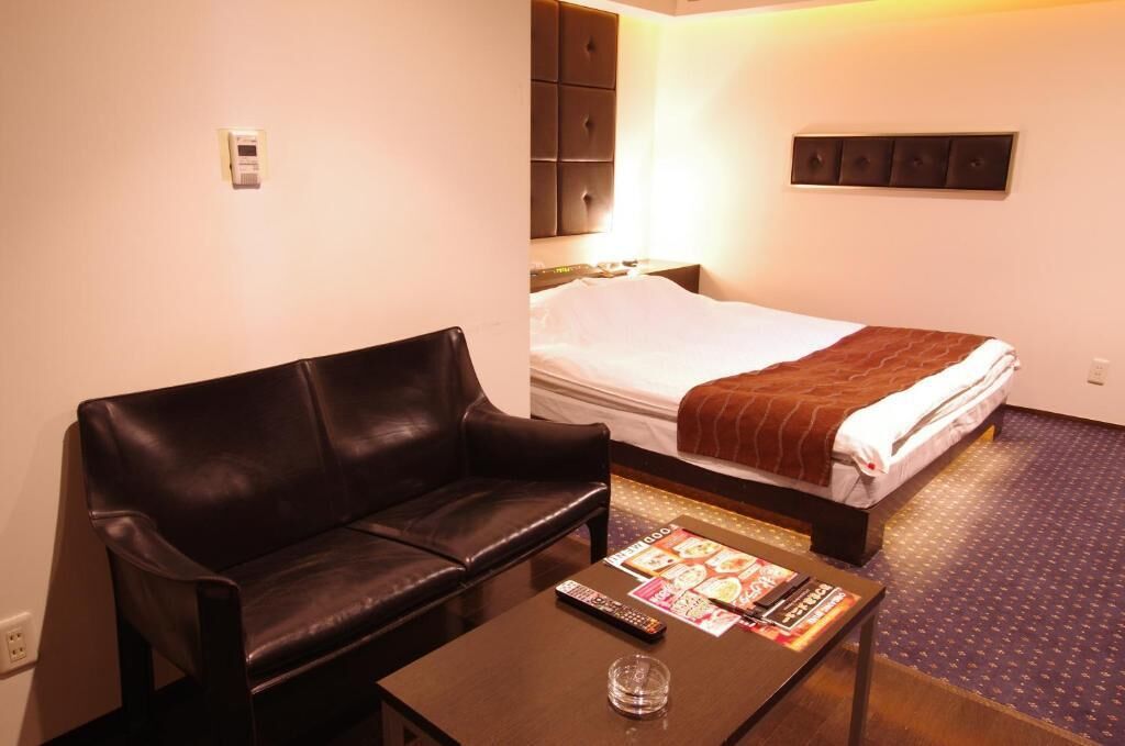A hotel room with a bed, a leather sofa, a small table with a remote control, and a magazine.