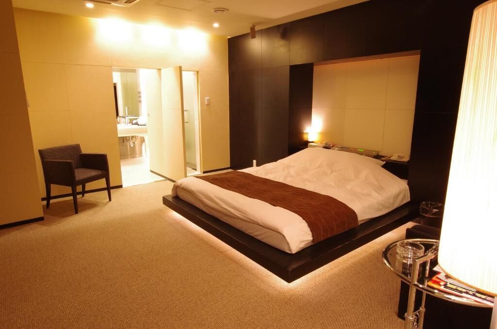 A hotel room with a bed, a chair, a bedside table, and a mirror.