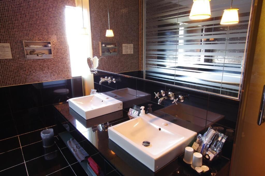 A modern bathroom with two sinks, a mirror, and a window with blinds.