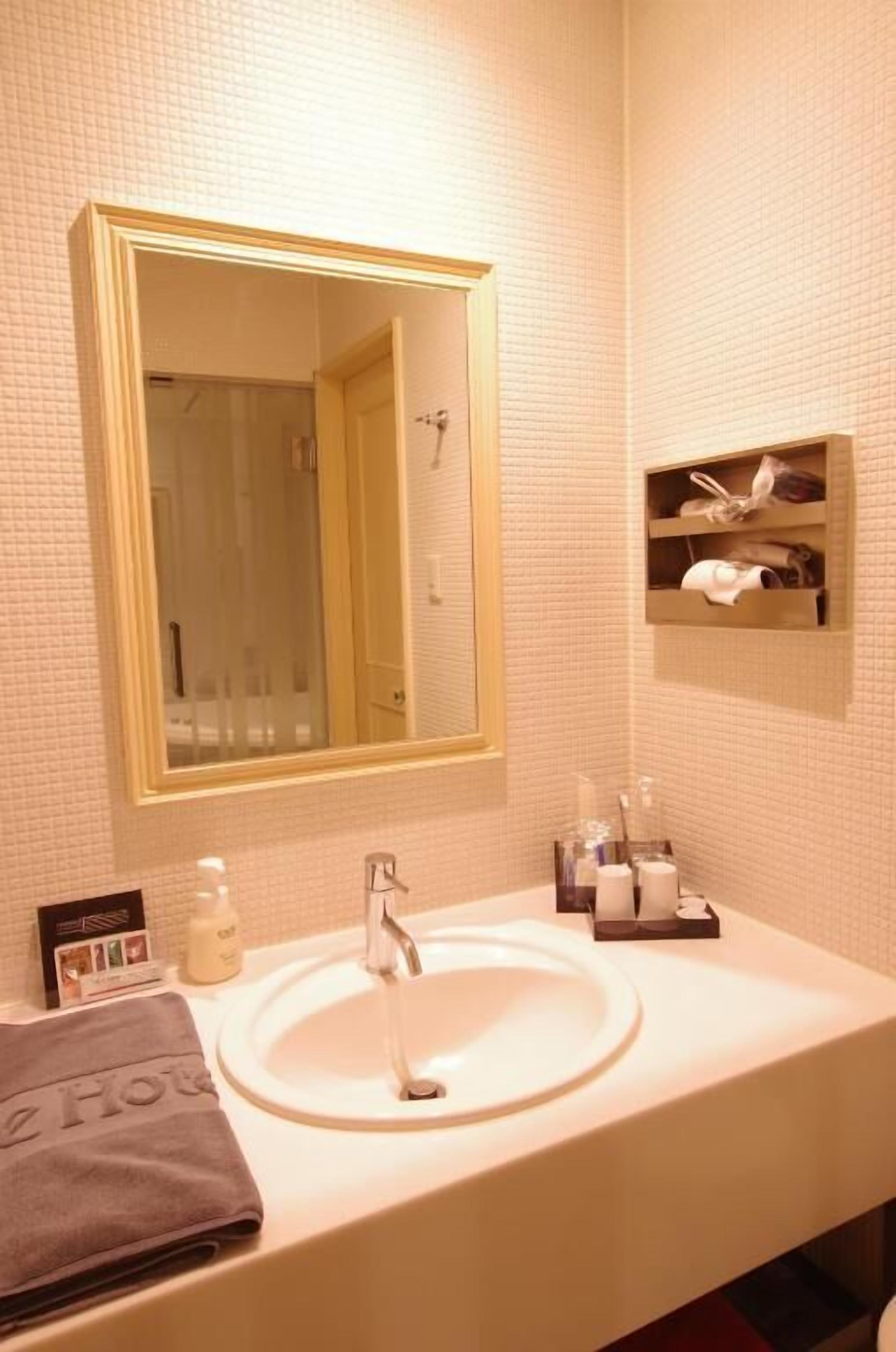 A bathroom with a large mirror, a sink, a towel, and a shelf with toiletries.