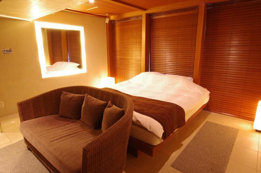 Une chambre à coucher avec un lit, un canapé marron, une fenêtre et des stores en bois.